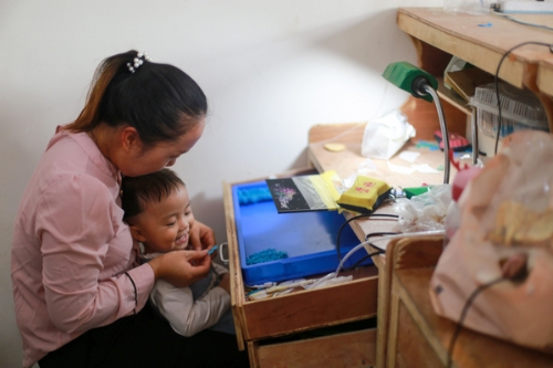 2021年8月9日，在貴州省黔西市綠化白族彝族鄉(xiāng)豐收村農(nóng)家車間里，村民一邊看娃一邊在加工首飾品。